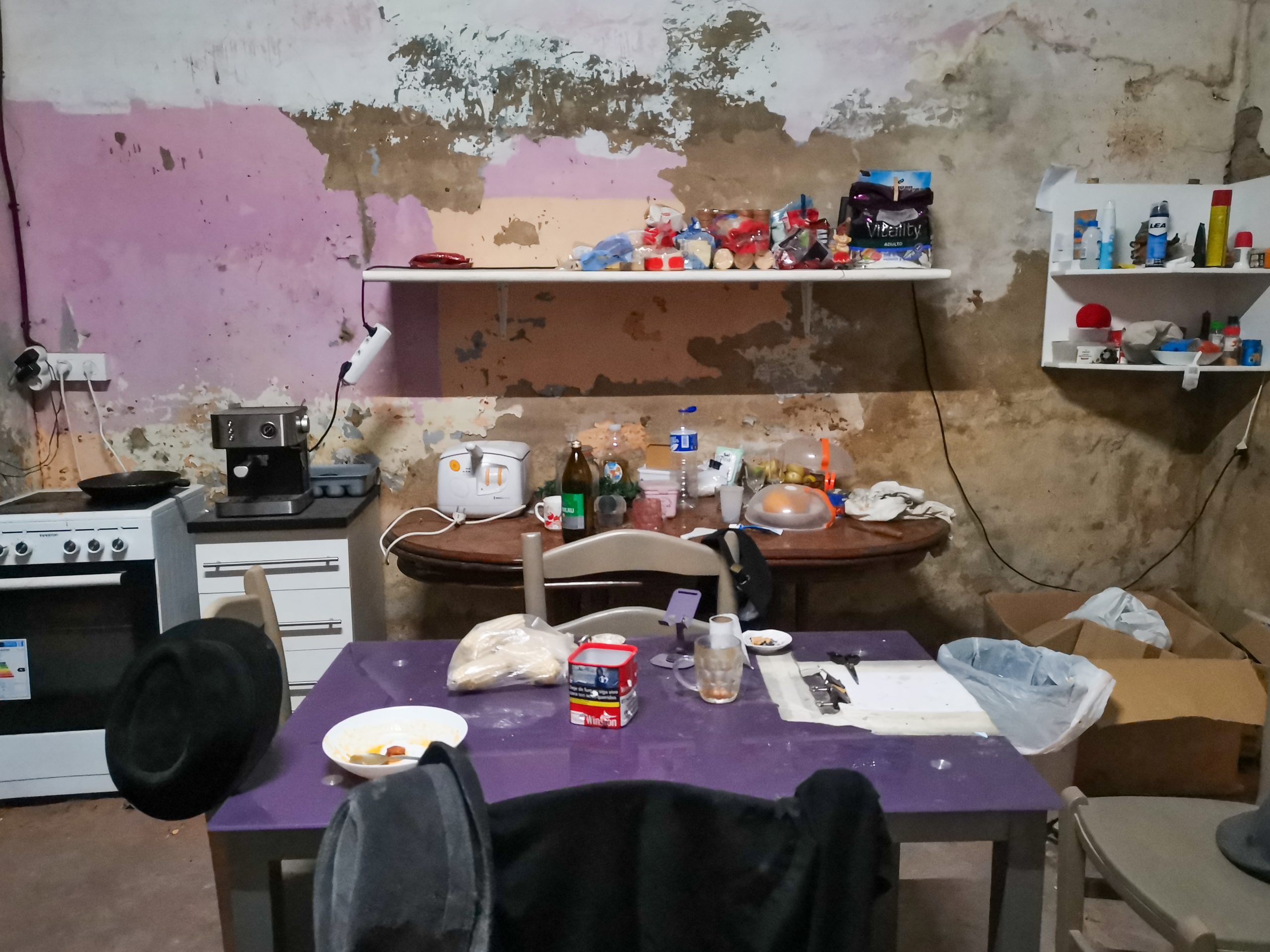 A damaged kitchen and dining area with peeling walls and scattered belongings inside a flood-affected home in Paiporta.